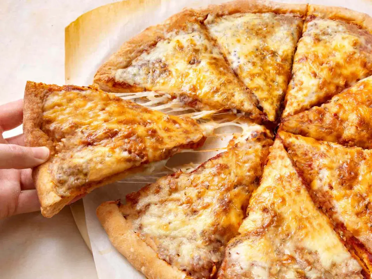 En hand lyfter en bit av en gyllene pizza med smält ost. Perfekt för en snabb pizzadeg-middag!