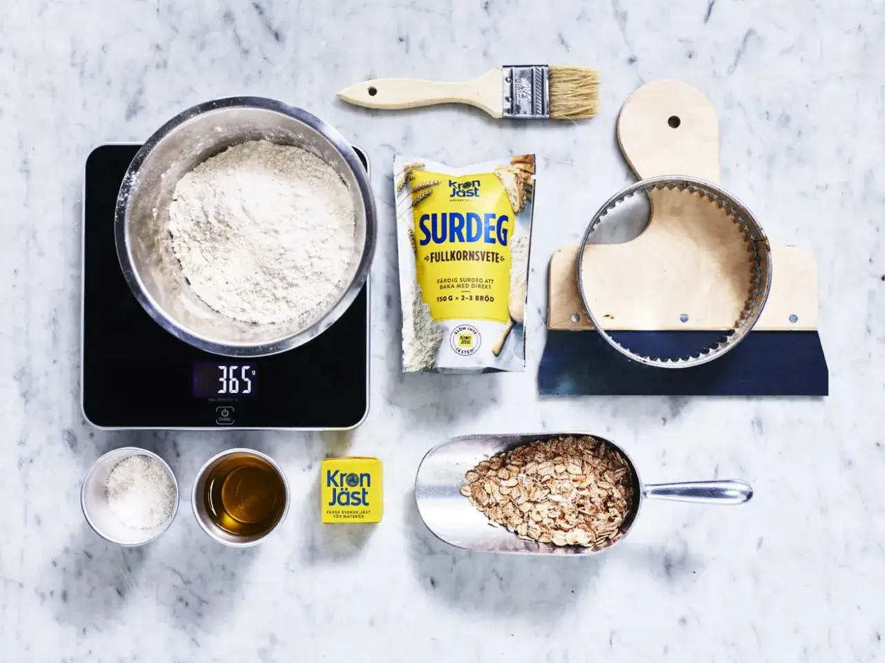 Ingredienser för surdegsbröd: mjöl i skål på våg, påse med surdeg, havregryn, olja, salt och jäst. Verktyg för bakning.