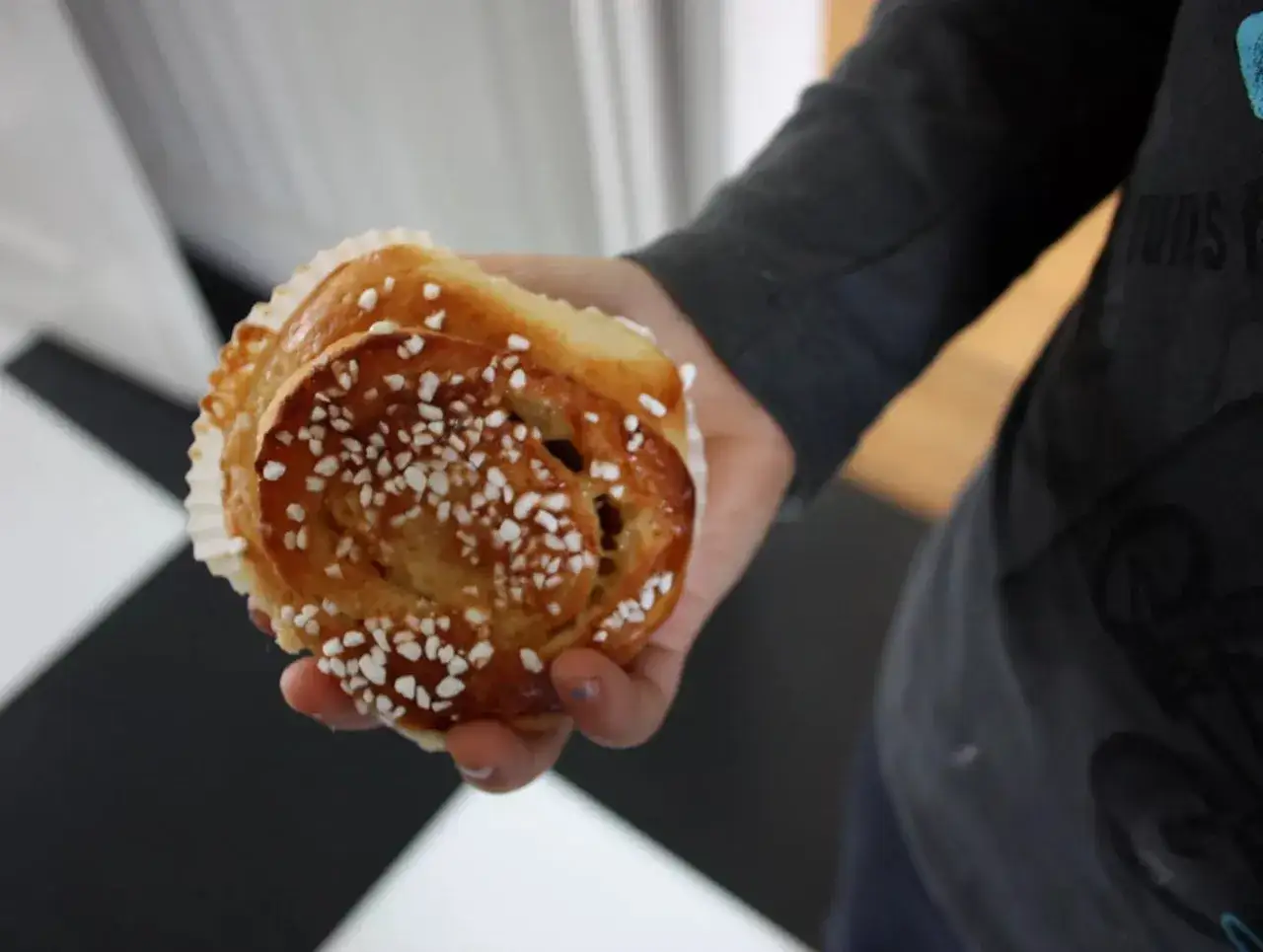 En hand håller en gyllene bulle med mandelmassa och pärlsocker. Perfekt för fikat!