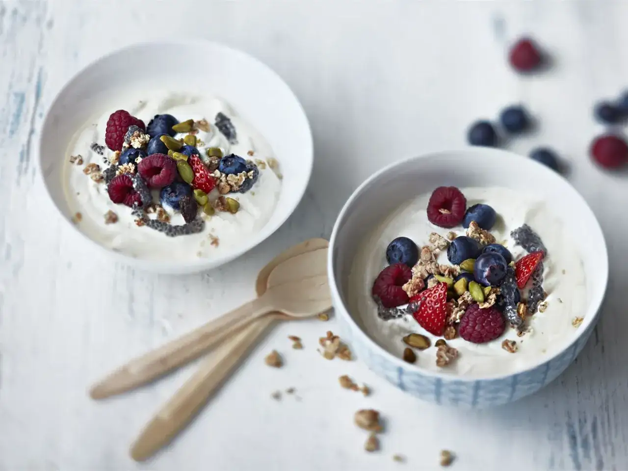 Två skålar med krämig fil yoghurt toppad med färska bär, granola och nötter. En hälsosam frukost eller mellanmål.