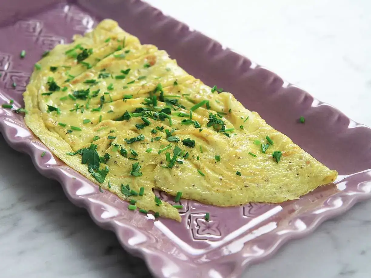 En fluffig omelett med gräslök, perfekt för ett snabbt omelett recept. Serveras på en lila tallrik.