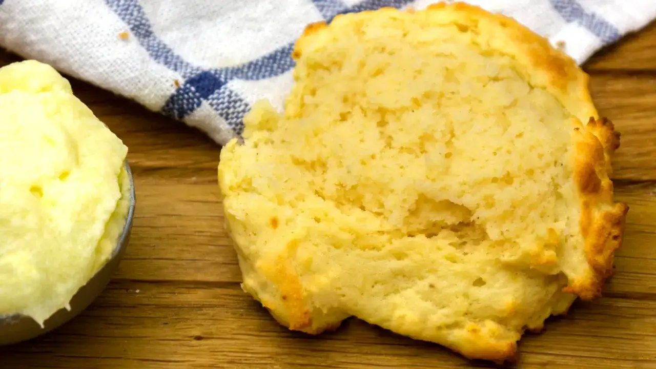 En fluffig scone bredvid en skål med krämigt, flytande margarin. En blåvitrandig kökshandduk ligger bakom.