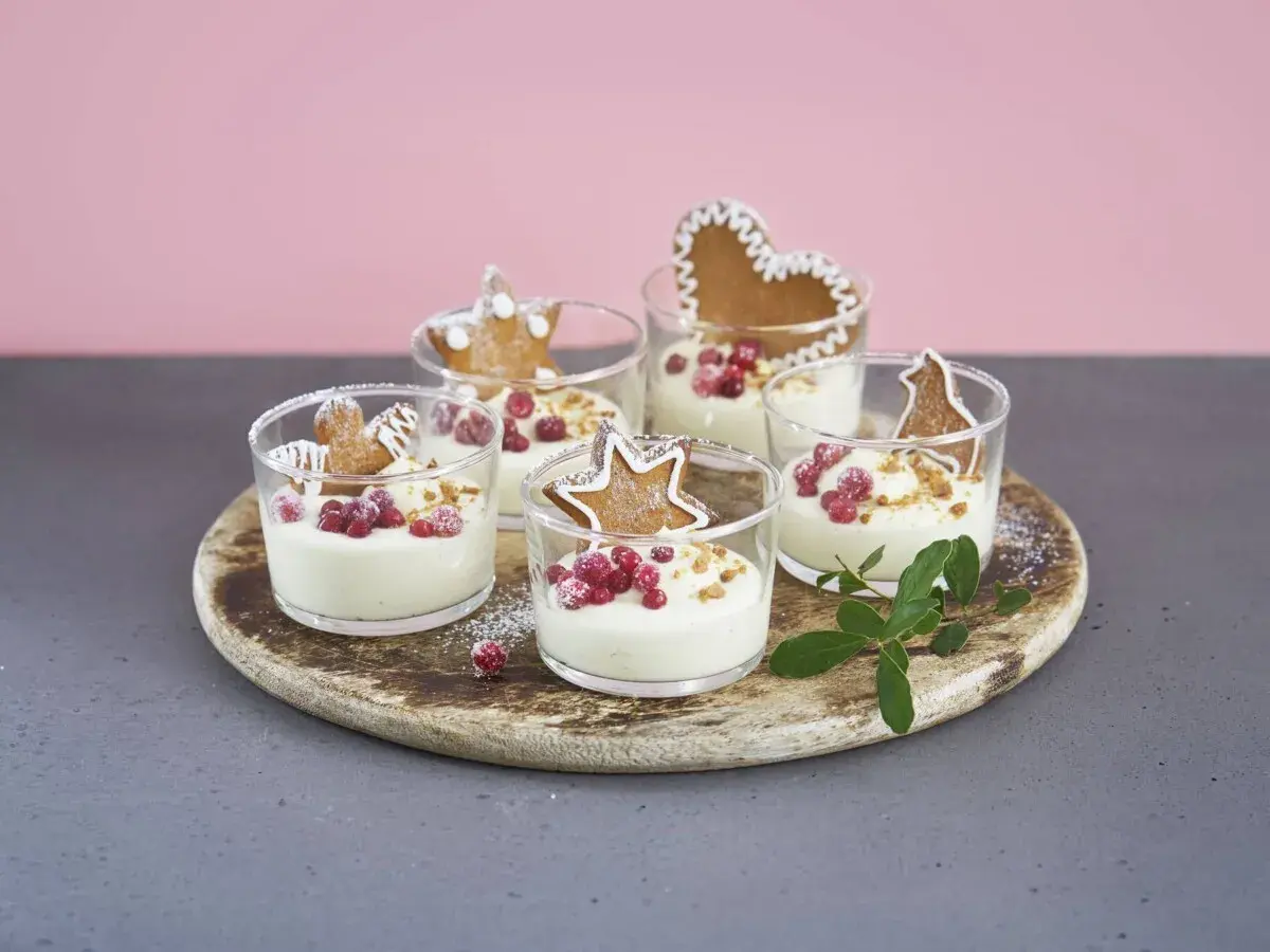 Fem små glas med krämig vit chokladmousse, toppade med lingon och pepparkaksfigurer. En festlig dessert!