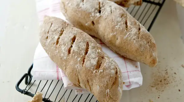 Två nybakade bröd, perfekta för ett skrädmjöl recept. Ligger på ett rutigt tyg på ett galler.