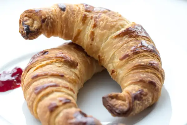 Två gyllene, krispiga croissanter på en vit tallrik med en klick sylt. Perfekt för ett croissant recept.