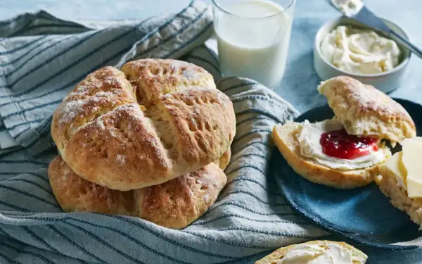 En hög med söta scones, redo att avnjutas med sylt och grädde. Ett glas mjölk står bredvid, perfekt för en mysig fika.