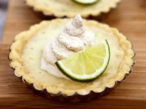 En liten citron key pie med en klick grädde och en limeklyfta.