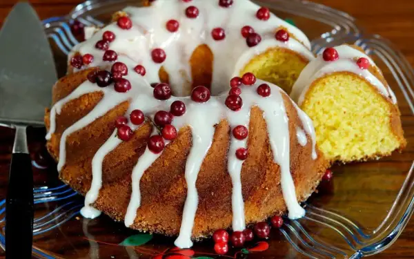 En gammaldags sockerkaka med glasyr och lingon. En bit är uppskuren och visar den gyllene insidan.