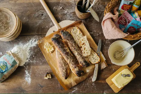 Nybakade surdegsbröd på en bakplåt, redo för ett gott surdeg recept. Ingredienser som mjöl och smör ligger utspridda.