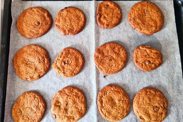 Tolv gyllene chocolate chip cookies utan farinsocker ligger på ett bakplåtspapper. De ser perfekta ut!