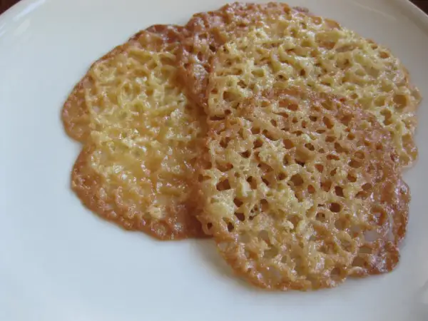 Tre gyllene havreflarn utan sirap ligger på en vit tallrik. De är tunna och krispiga med ett vackert nätmönster.