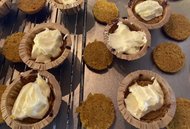 Små morotskakor i pappersformar, några med krämig frosting, redo att frysa in morotskaka för senare njutning.