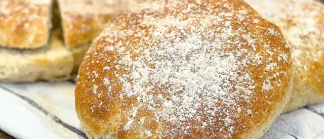 Nybakade skons, pudrade med mjöl, ligger på en randig kökshandduk.