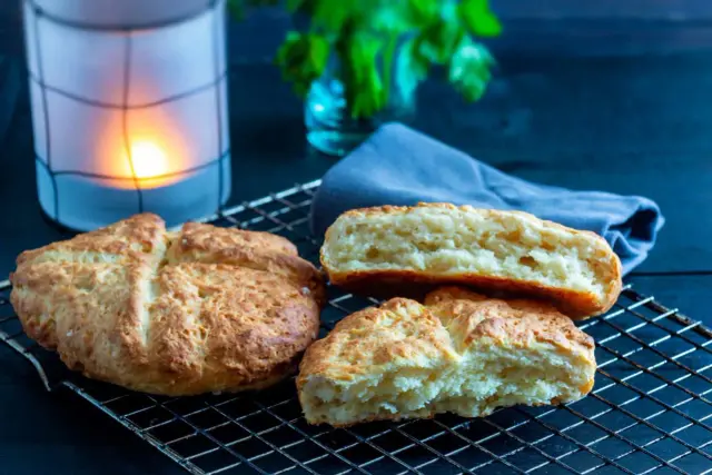 Njut av nybakade, klassiska scones på ett galler. En ljuslykta och en blå duk skapar en mysig stämning.