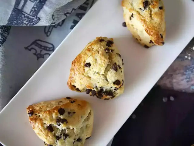 Tre gyllene chokladchipsscones på en vit bricka, redo att avnjutas. Ett perfekt scones recept för fikat.