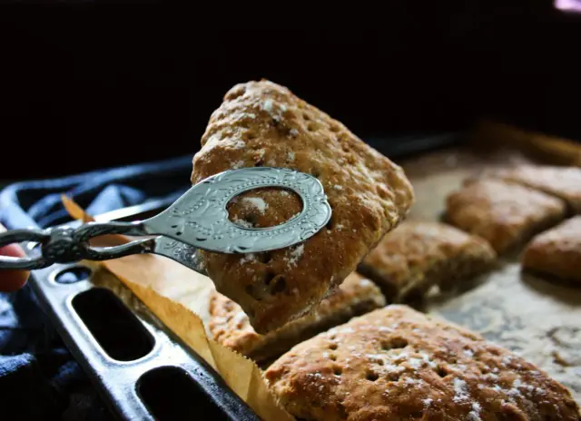 Nybakade scones, perfekta att baka med filmjölk, tas upp ur formen med en fin tång.