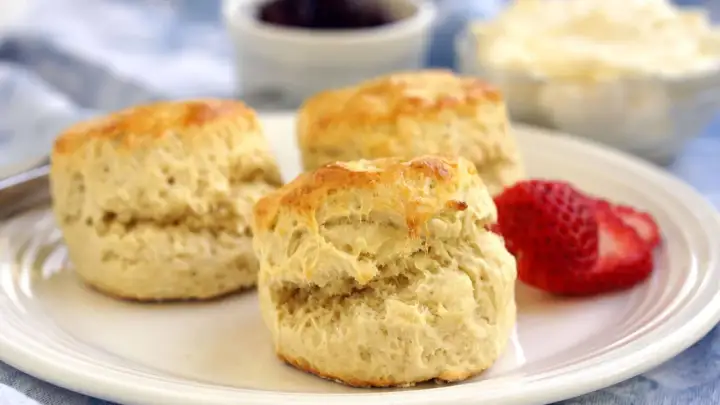 Tre fluffiga scones, ett perfekt scones grundrecept, serveras med jordgubbar och grädde.